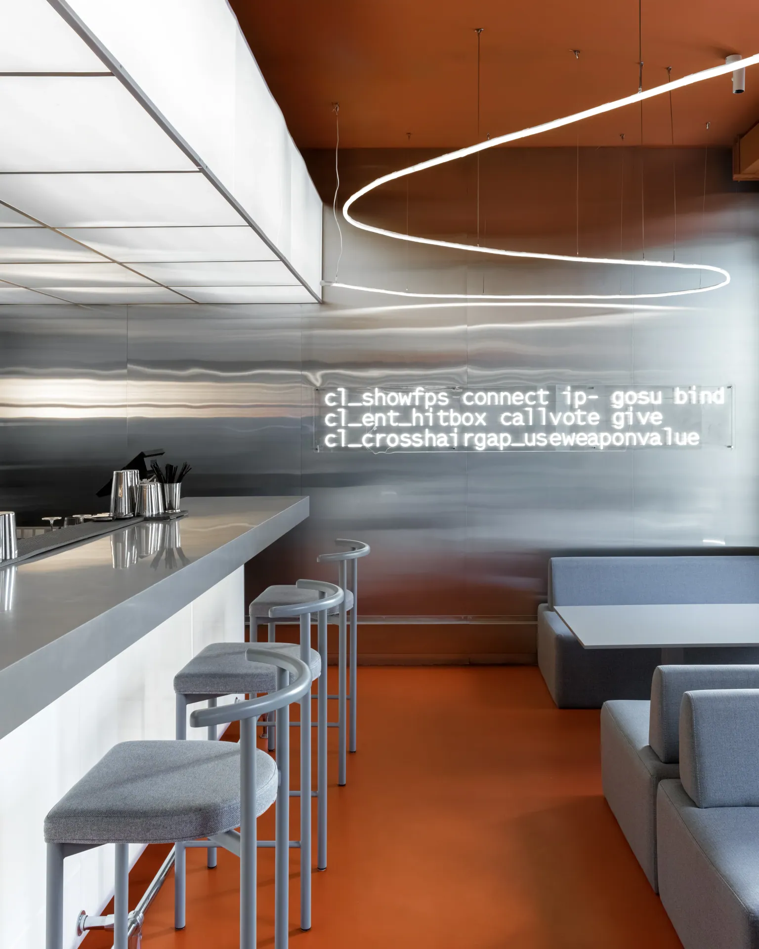 Bar counter with grey stools beneath a ring-shaped luminaire
