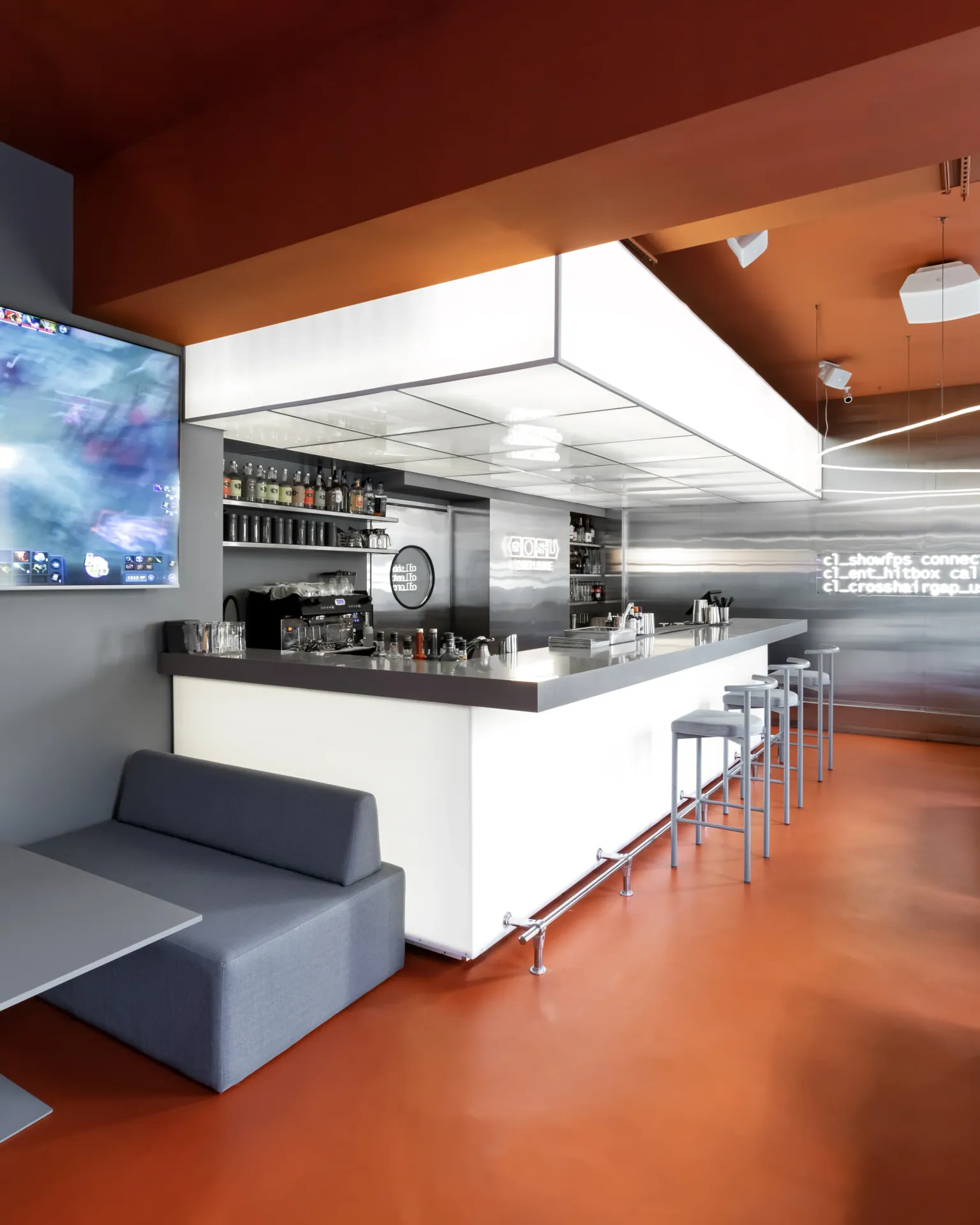 White bar front with grey sofa seating and a wall-mounted screen
