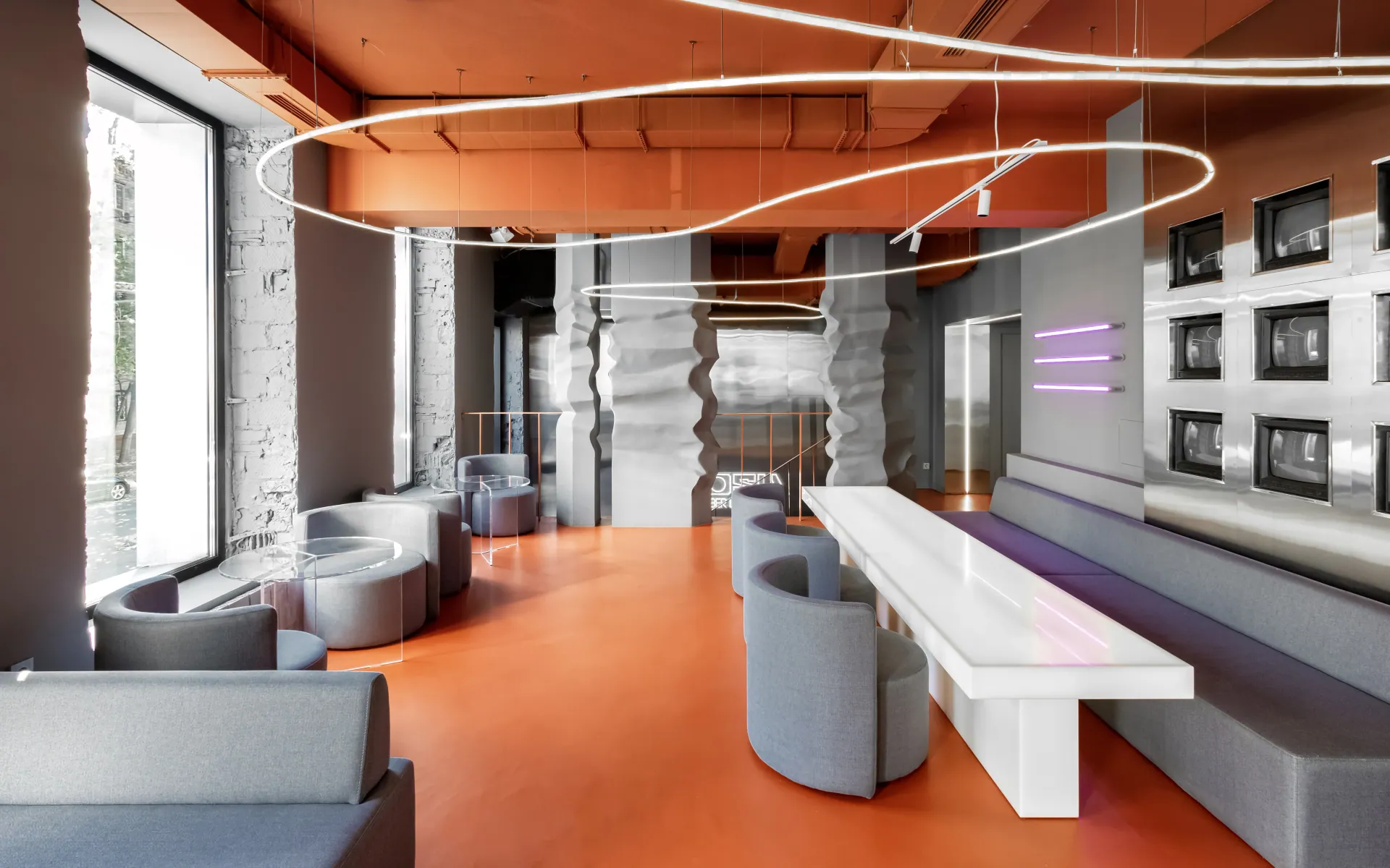 GOSU Cyber Lounge: ring luminaires, sculpted columns, a screen wall and a long white table over an orange floor