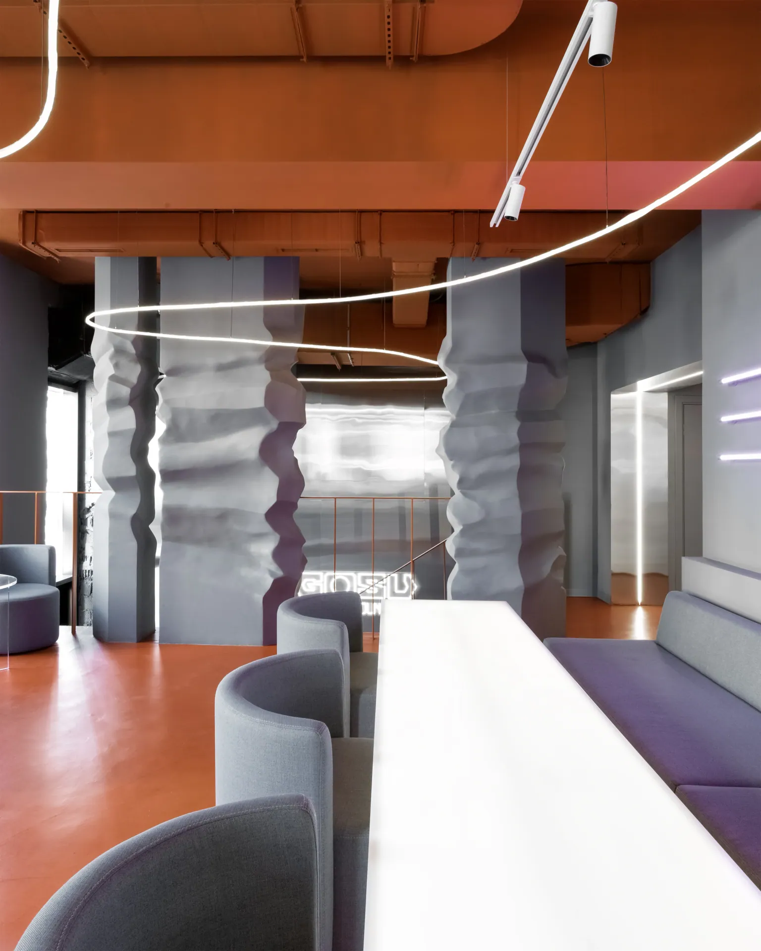 Ring luminaires and sculpted columns above the lounge, with a track light in the foreground