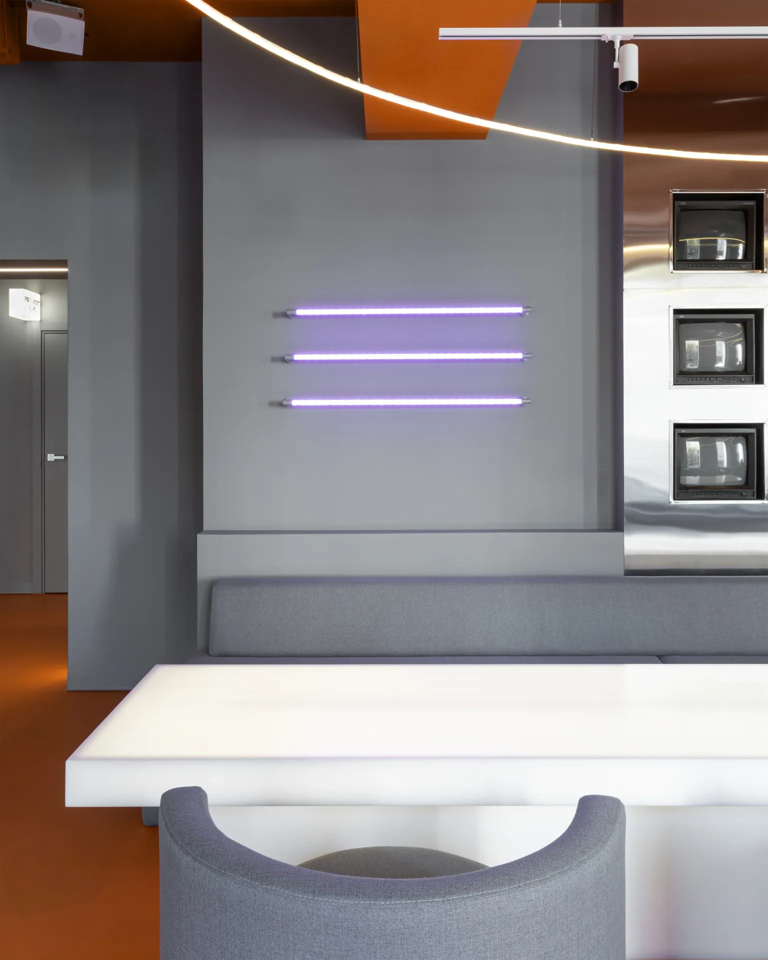 Violet linear lights on a grey wall above a long white table and grey armchairs