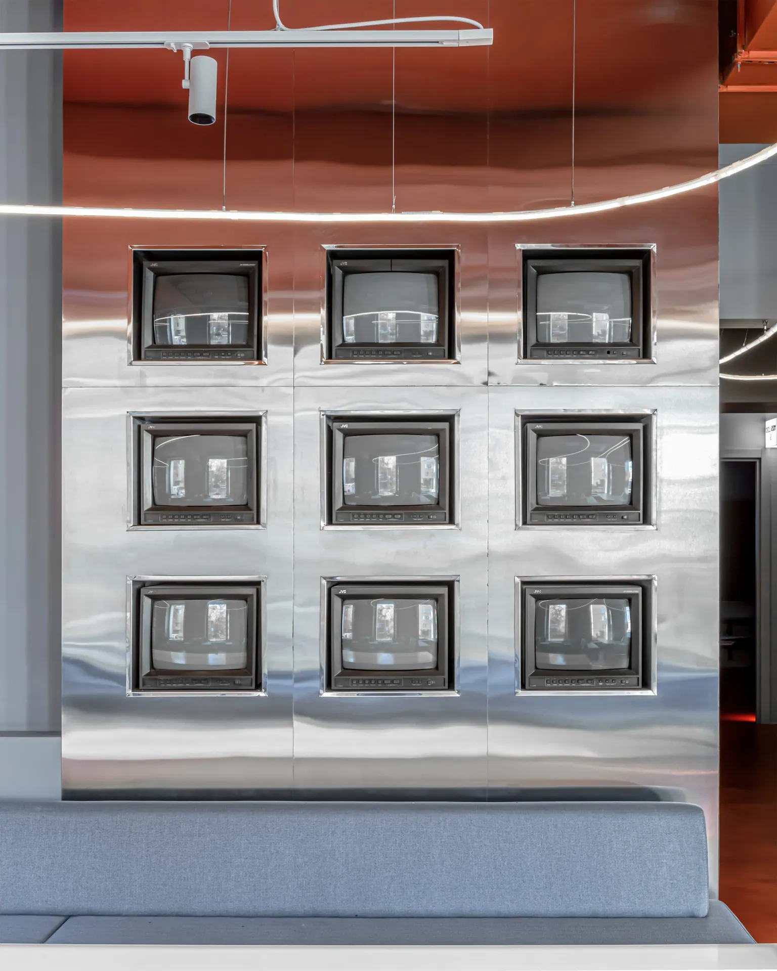 Wall of nine framed screens set in mirror-finish metal, above a grey banquette