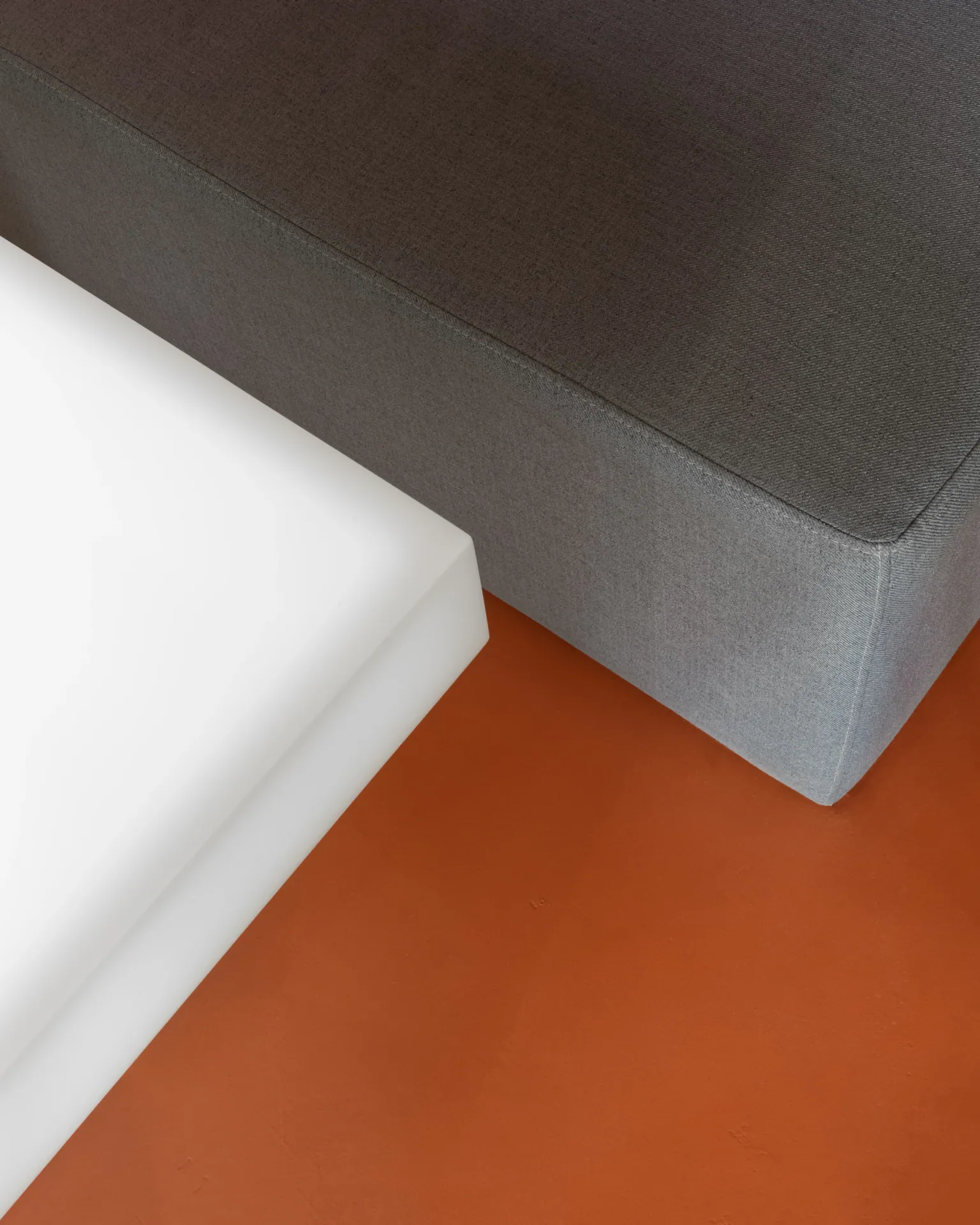 Detail of a white table edge, grey upholstery and orange floor